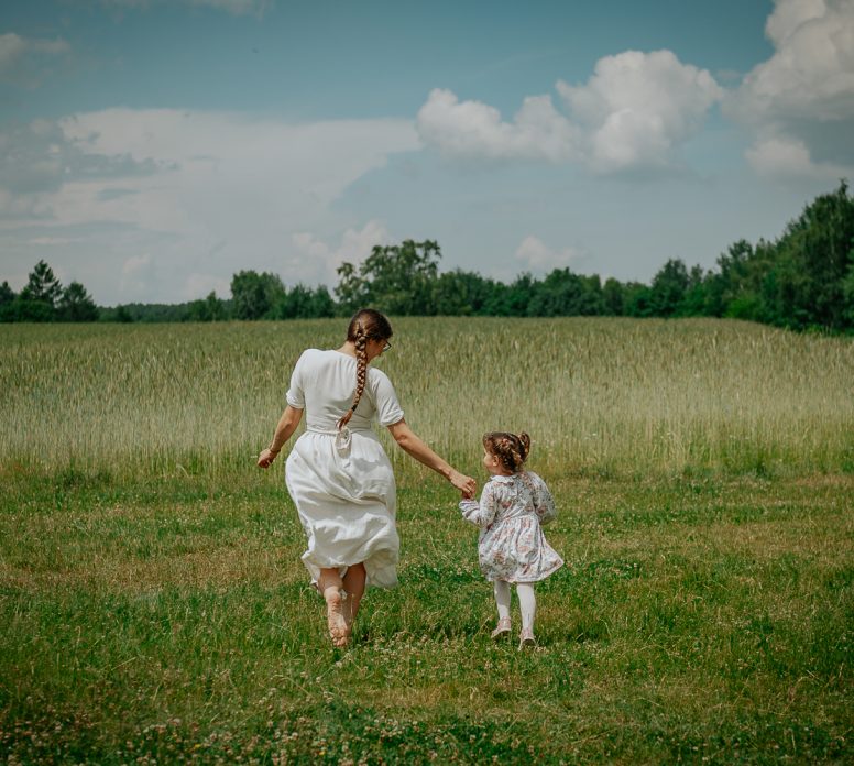 mama idąca z małym dzieckiem przez łąkę podczas sesji rodzinnej