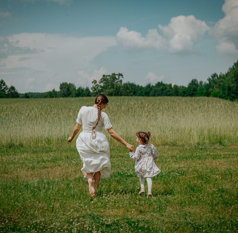 mama idąca z małym dzieckiem przez łąkę podczas sesji rodzinnej