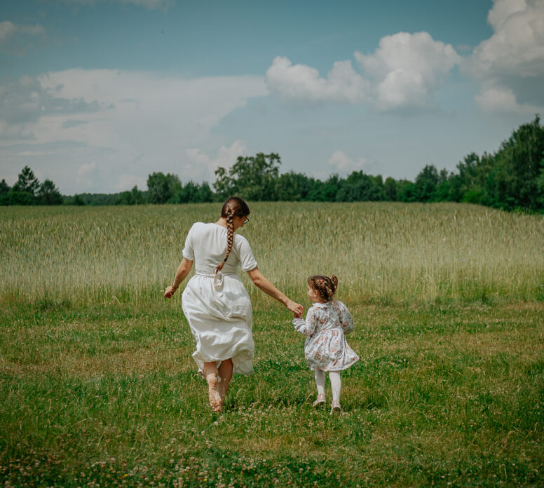 mama idąca z małym dzieckiem przez łąkę podczas sesji rodzinnej